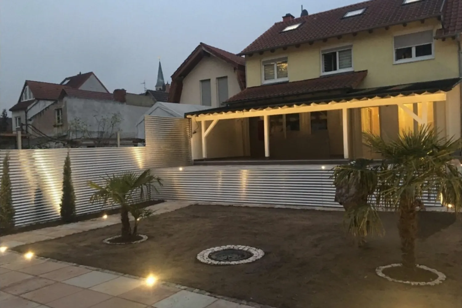 Nachher: neu gestalteter Garten mit Terrasse, Sichtschutz, Palmen und LED-Beleuchtung bei Dämmerung