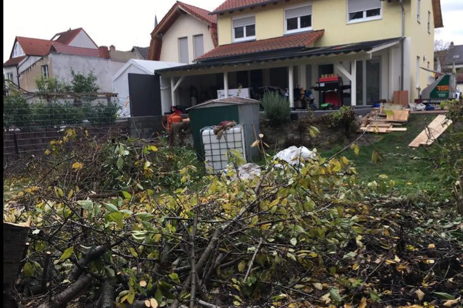 Vorher: überwuchertes Grundstück mit Rückschnittgut vor dem gelben Haus